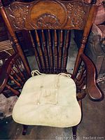 Wooden rocking chair with carved backrest and beige tie-on cushion.