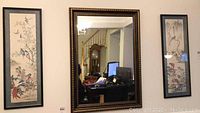 Photo showing the large framed mirror centered between two vertical framed bird prints on the wall.