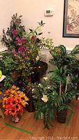 Photo showing metal bar cart surrounded by various faux flower and leaf arrangements of different heights and colors.