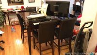Photo showing dark brown wooden high table with glass centerpiece and 4 faux leather stools around it in a room with hardwood floor.
