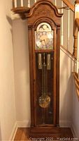 Full front view of the oak grandfather clock showing carved arch-top and glass front
