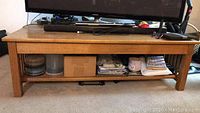 Front view of the low wooden table with items on bottom shelf and a TV on top.