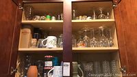 Cabinet shelves showing multiple glassware types including wine glasses, mugs, and shot glasses visible through glass cabinet doors