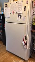 View of the full white Kenmore refrigerator from the front showing top freezer door and bottom refrigerator door with papers and magnets attached.