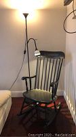 Wooden rocking chair with black painted finish next to black floor lamp with white shade, positioned against wall on wood floor
