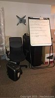 Overall view of the black office chair, paper shredder on floor, and flip chart easel with paper pad.
