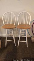 Front view of two wooden counter chairs side-by-side with natural wood seats and white painted backs and legs.