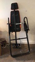 Front view of a black and orange inversion table with padded headrest, armrests, footrest with straps, and sturdy metal frame.
