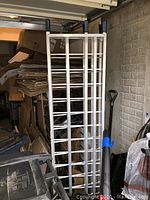 Folded metal aluminum truck ramp stored upright beside stacked cardboard boxes and other tools.
