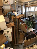 Photo showing chrome storage rack with boxes and packing materials around it in a garage or storage space, rack with wire shelving and vertical chrome poles.