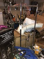 Full view of the chromed metal clothes storage rack showing wire mesh shelf, vertical poles and horizontal bars for hanging clothes, surrounded by boxes and other stored items.