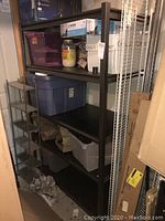 Full view of the metal utility shelf with various items stored on it including plastic storage bins and miscellaneous boxes.
