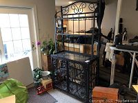 Full view of black painted metal wrought iron bar with marble shelves showing decorative scrollwork and storage cabinets below.