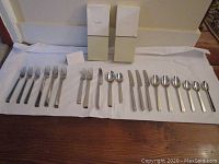 Overview of all 20 flatware pieces laid out with two original Kate Spade boxes behind, showing the full service for 4 in five-piece settings.