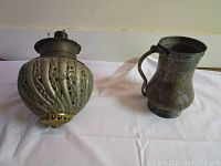 Photo of the oil lamp part with decorative metal reservoir and wick in the base, alongside hammered copper pitcher