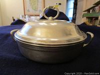 Side view of the pewter casserole dish and lid showing the decorative handle on the lid and one handle on the dish