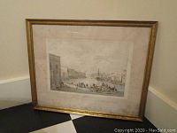 Framed antique lithograph showing a wide angle view of the dockyard with buildings and ships, leaning against a wall.