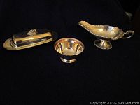 Group photo of all three silver plate items together on black background: covered butter dish with lid and glass insert, silver bowl, and ornate gravy boat