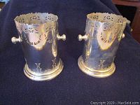 Two metal wine coolers with reflective silver-tone finish and decorative cut-outs, shown together on a dark fabric background.