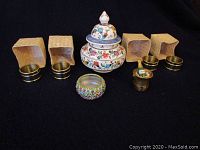 Photo showing Limoges floral trinket box and four brass napkin rings with beige textured boxes plus small colorful decorative item