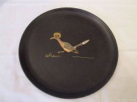 Black round tray featuring a painted bird design in tan and white on the center, placed on a white background.