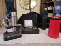 Lot arranged on table showing three thermoses and two corkscrew sets. Background includes mirror and furniture.