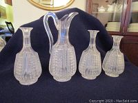 The set of one pitcher and three matching carafes on a dark fabric background, showing the clear cut glass with geometric pattern.