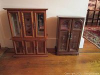 Two wooden music boxes of different sizes, visible compartments and glass doors, placed on a wooden floor