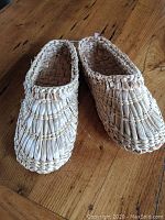 Pair of woven straw footwear with textured upper and red interior sole lining, displayed on wooden surface.