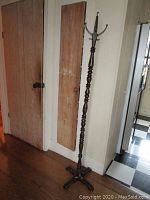 Full view of tall wooden coat rack standing against a wall, showing its height and base design.