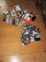 Overall view of remotes, cables, cell phones, and accessories laid out on floor.