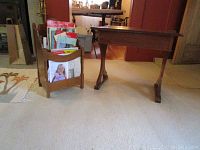 Wooden table and wooden magazine rack shown side by side on carpeted floor in a room, magazine rack holding magazines and other papers.