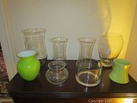 Seven assorted glass vases arranged on a dark wood surface, showing color, size and variety