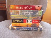 Stack of VHS and DVD tapes including Hope Floats, Tous les matins du monde, Archives of War, TDK HS T-160 blank tape, and Riverdance.