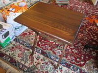 Single wooden TV tray fully opened showing tabletop and folding legs on patterned carpet.