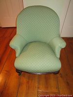 Front view of upholstered green accent chair showing fabric, curved back and carved wood base.