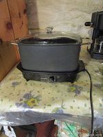Full view of black rectangular slow cooker with glass lid and side handles on floral tablecloth.
