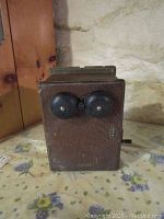 Front view of antique wooden ringer box with two black metal bells and metal winding key on side.