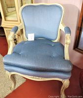 Front view of vintage Victorian style wood chair with blue fabric upholstery. Cushion and armrests padded, wooden frame painted off-white with distressed look.