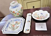 Photo showing four china items on a wooden surface: a floral ginger jar with lid, a square floral plate, a long narrow dish with small floral motifs, and a scalloped dish with butterfly and floral decoration.