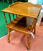 Photo of mid-century modern light brown wood square side table with turned legs and lower shelf, showing normal wear.