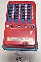 Front view of red 1950's Wolverine tin adding machine showing numbered keys, total display windows, and minor rust spots.