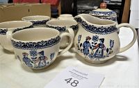 Five cream-colored ceramic cups with blue intricate border patterns near rim and painted couple floral design, arranged around sugar bowl and creamer on a flat surface.