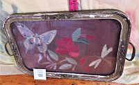 Full view of vintage wooden tray featuring a butterfly, dragonfly, and red flowers on fabric background encased in glass, showing metal handles and wear.