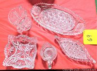 Full view of the five-piece vintage clear pressed glassware set on a red cloth background showing the oval tray, two serving dishes, mini vase, and creamer from top angle.