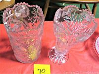 Photo of two vintage cut glass vases showing the detailed floral and sunburst patterns with scalloped rims, set on a red surface.