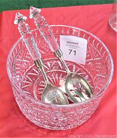 Glass serving bowl with spoon and fork inside on red cloth background