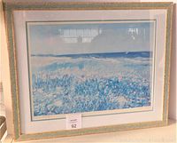Full front view of the framed print showing the coastal landscape artwork in blues and whites, mounted and framed with visible reflections on the glass.