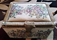 Closed rectangular vintage sewing box, woven and embroidered with pastel floral design on lid and sides.