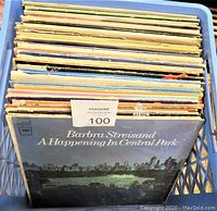 Photo showing a blue crate filled with a stack of vintage LP record albums. The album on front is Barbra Streisand - A Happening in Central Park with visible wear on the cover.
